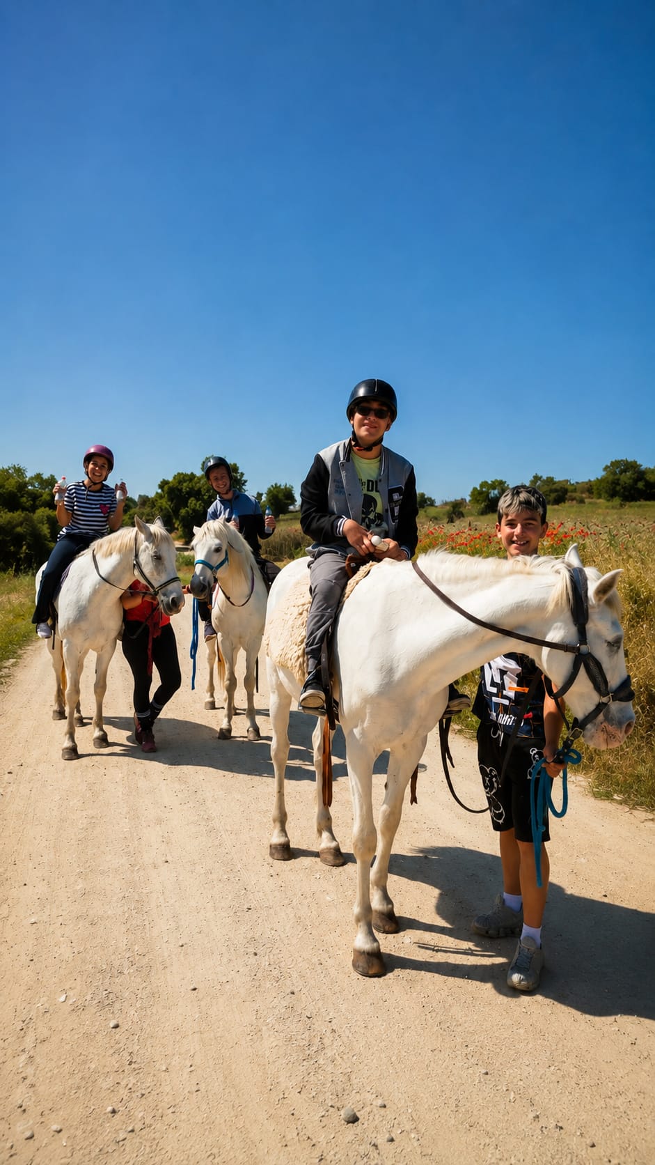 Grupo de jóvenes montando caballos blancos por un camino de tierra en un día soleado