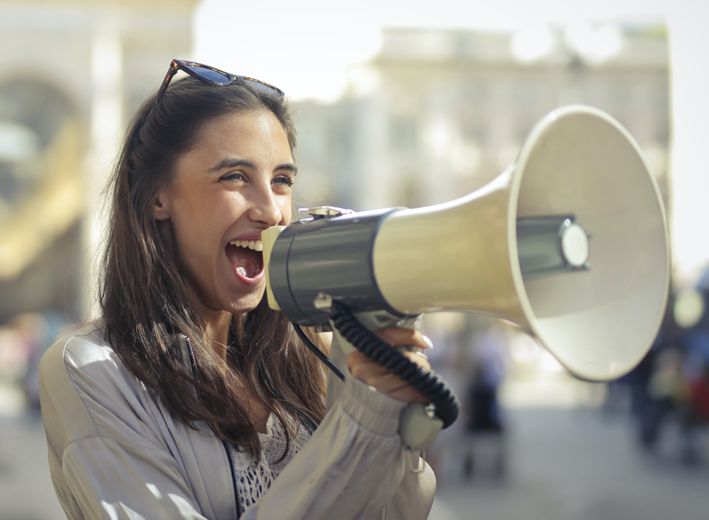 Mujer sonriente hablando por un megáfono en la calle
