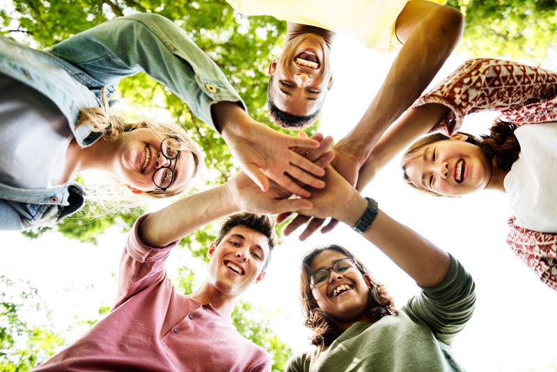 Grupo de jóvenes sonrientes juntando las manos en el centro bajo los árboles